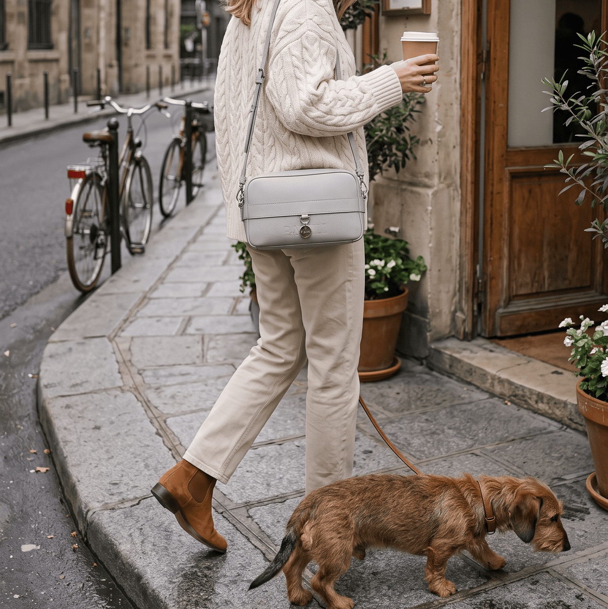 Eine junge Frau spaziert mit ihrem Dackel und einem Coffee to go durch die Innenstadt.