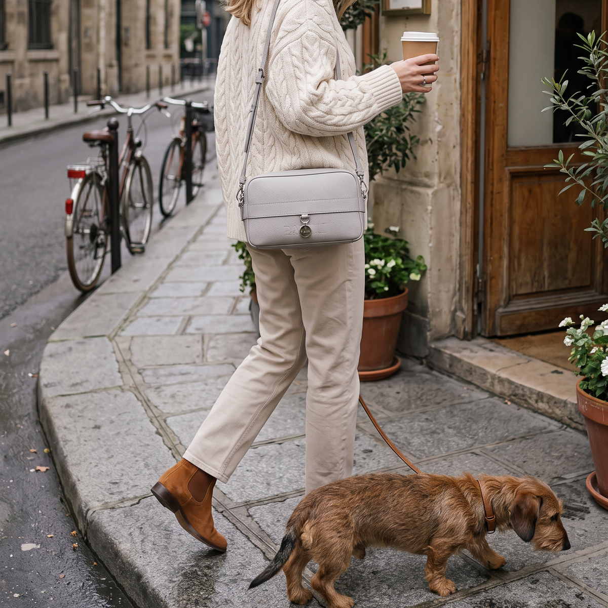 Eine junge Frau spaziert mit ihrem Dackel und einem Coffee to go durch die Innenstadt.