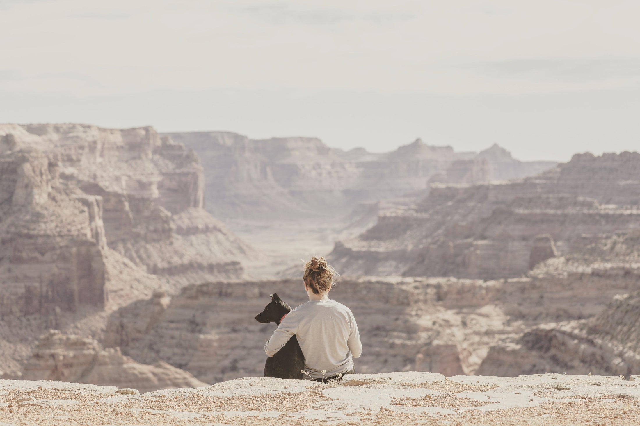 Woman hugging a black dog and overlooking canyons.